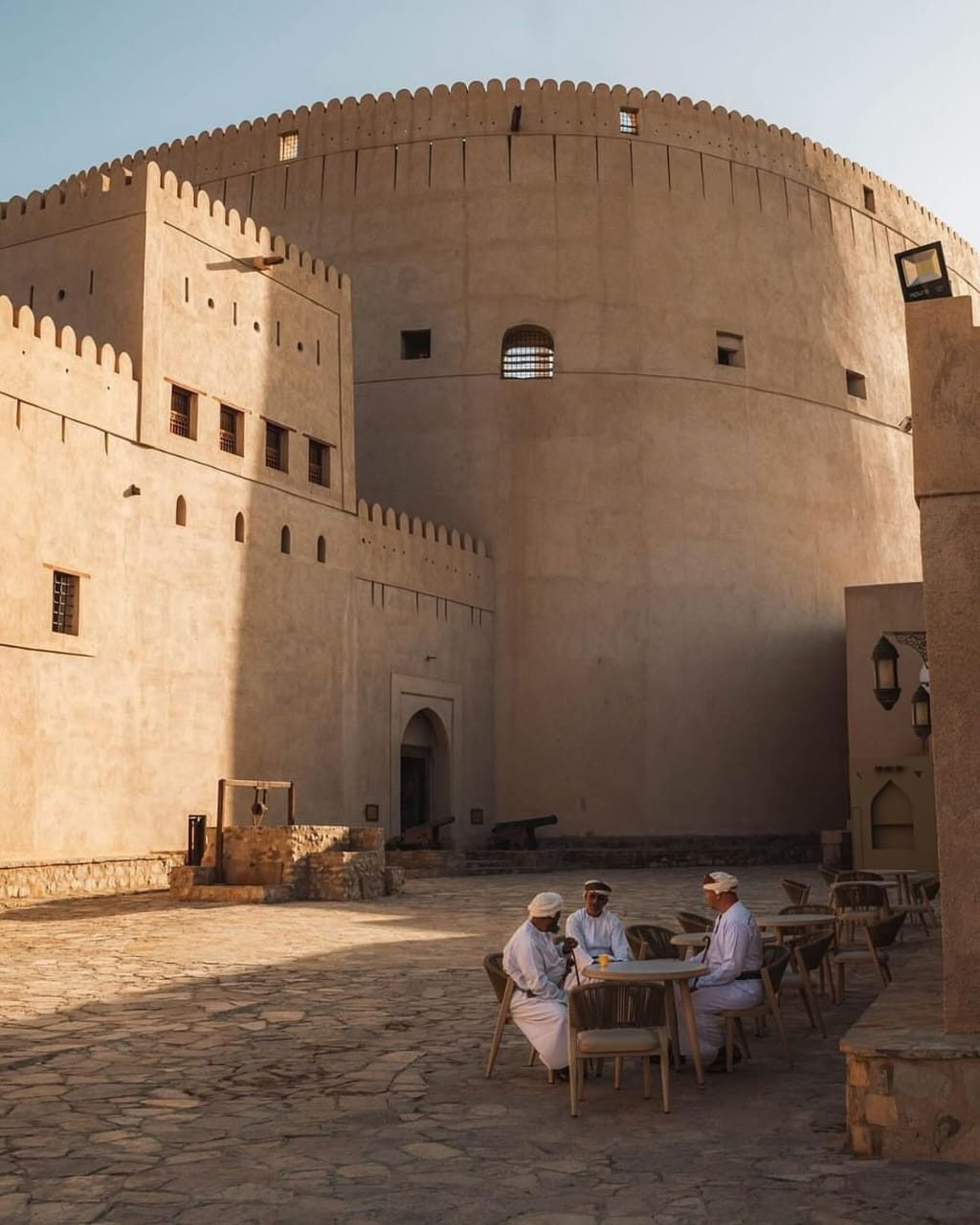 Trois hommes en dishdasha partagent un café dans la cour du fort de Nizwa