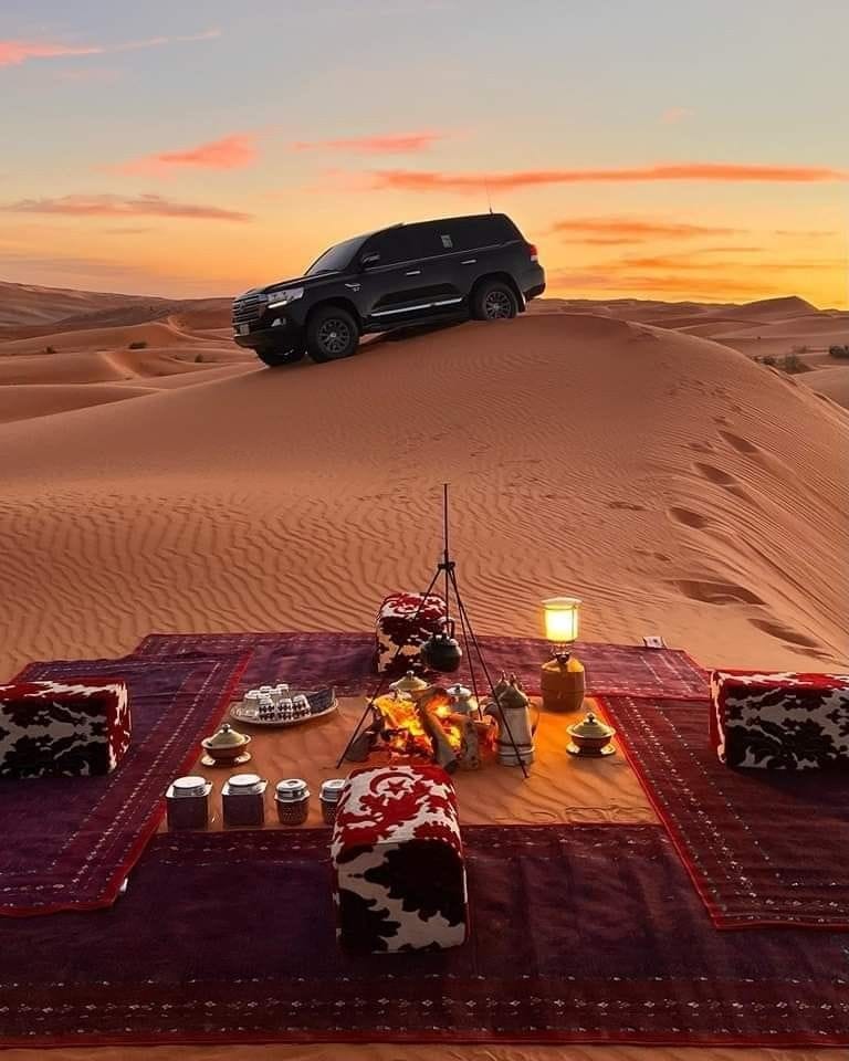 Un campement privé dressé sur une dune au coucher du soleil : tapis, café et feu